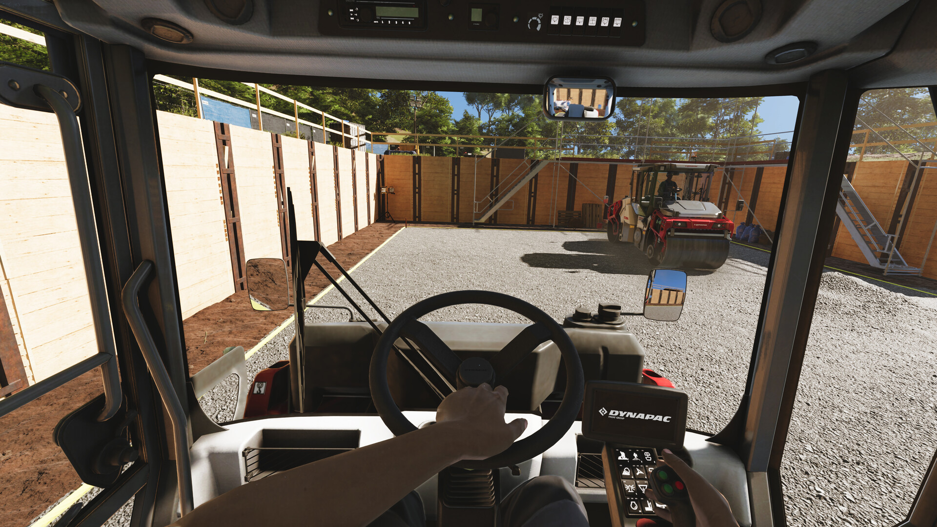 Blick aus einem Traktor auf eine Baustelle mit einem Walzenzug und Holzwänden.