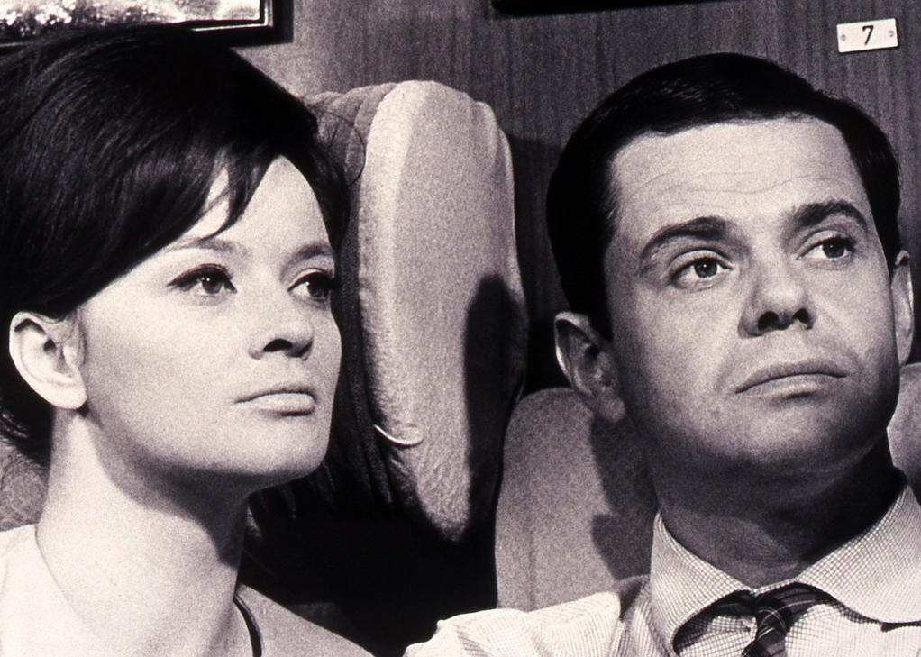 Schwarz-Weiß-Foto zweier Personen im Flugzeug, Mann und Frau schauen nach oben.