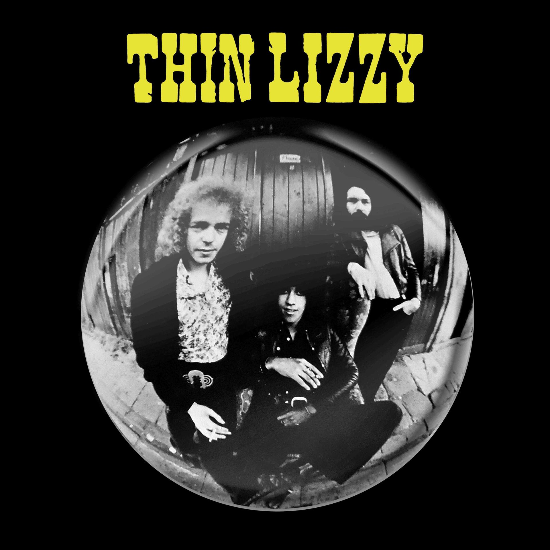 Drei Männer posieren vor einer Holztür, "THIN LIZZY" steht gelb darüber.