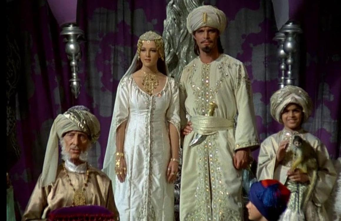 Vier Personen in traditioneller Kleidung mit Turbanen, eine Frau im weißen Kleid und ein Mann im hellen Gewand.