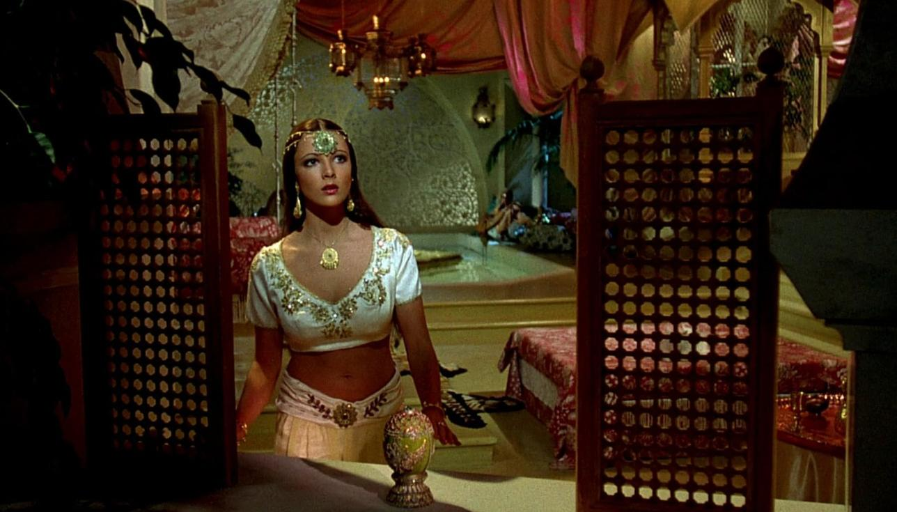 Eine Frau in orientalischer Kleidung steht in einem opulenten Raum mit Wasserbecken und Lampen.