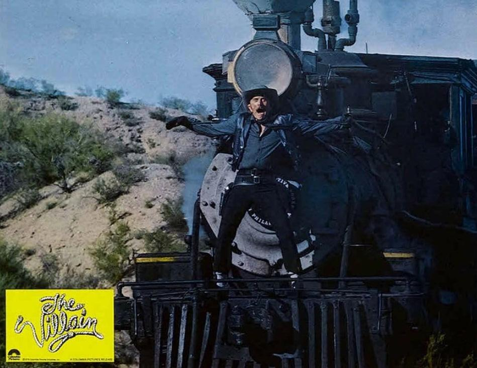 Ein Mann in einem Hut und dunkler Kleidung steht auf einer Dampflokomotive.