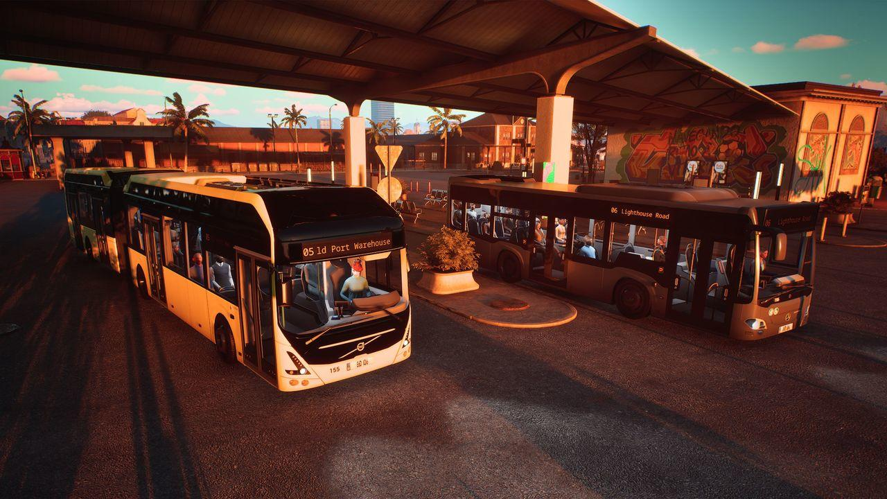 Zwei Busse unter einem Vordach, einer gelb, der andere dunkelgrau. Palmen im Hintergrund.