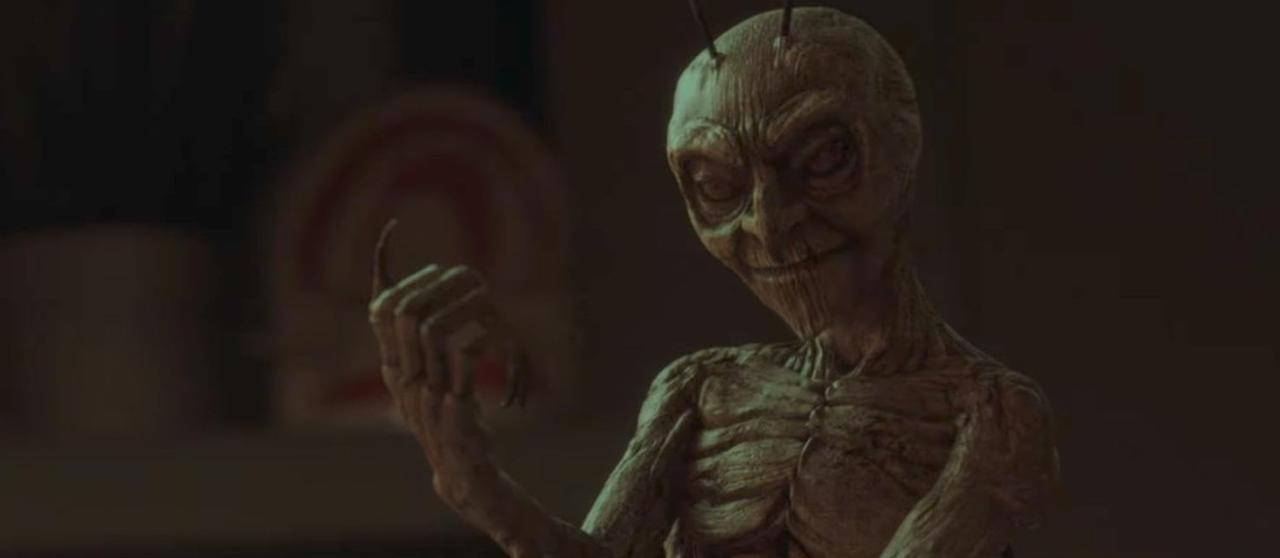 Eine gruselige, abgemagerte Alien-Figur mit großen Augen und einem finsteren Lächeln.