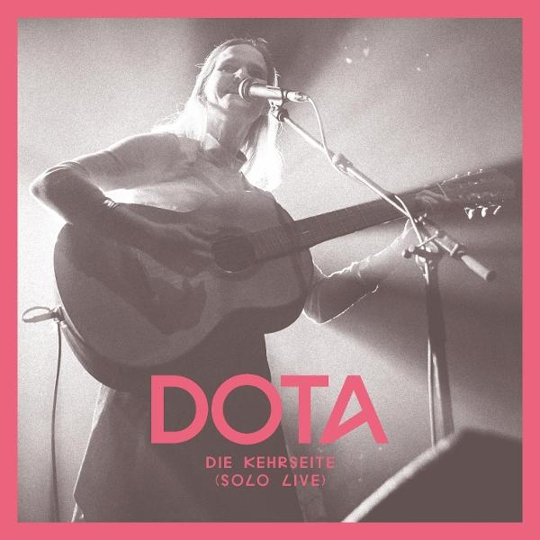 Eine Frau singt in ein Mikrofon und spielt Gitarre. Der Text 'DOTA' ist sichtbar.
