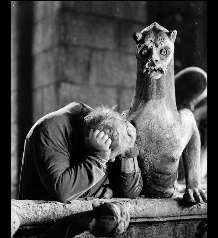 Ein Mann mit dem Kopf in den Händen neben einer gargoyle-ähnlichen Statue.