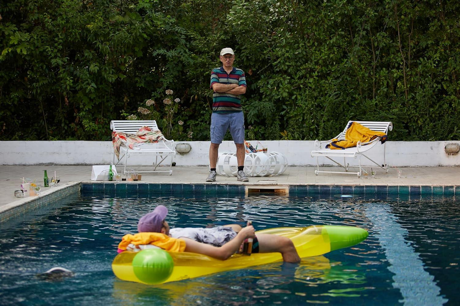 Mann auf gelber Luftmatratze im Pool, Mann steht am Beckenrand.