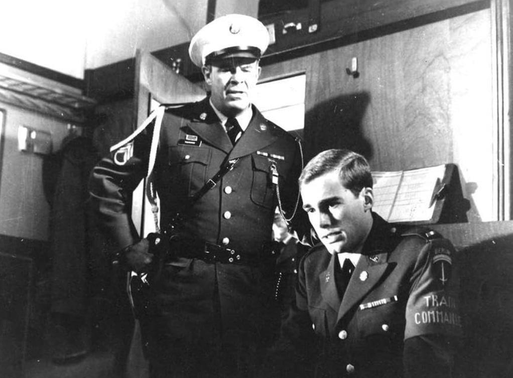 Ein Soldat in Uniform steht neben einem Mann in Uniform, der eine Armbinde trägt.
