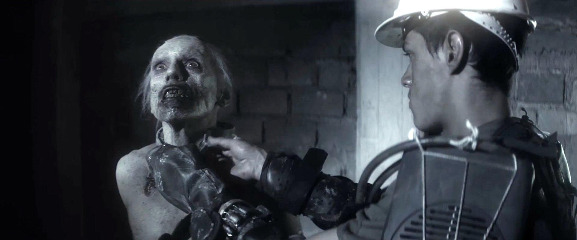 Ein Mann mit Helm berührt den Hals eines Zombies. Dunkle Szene.