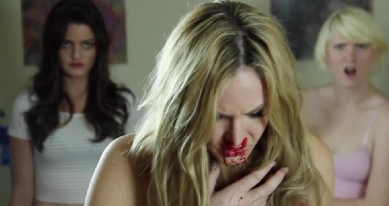 Eine Frau mit blutigen Lippen und Nase hält sich die Brust. Zwei andere Frauen stehen im Hintergrund.