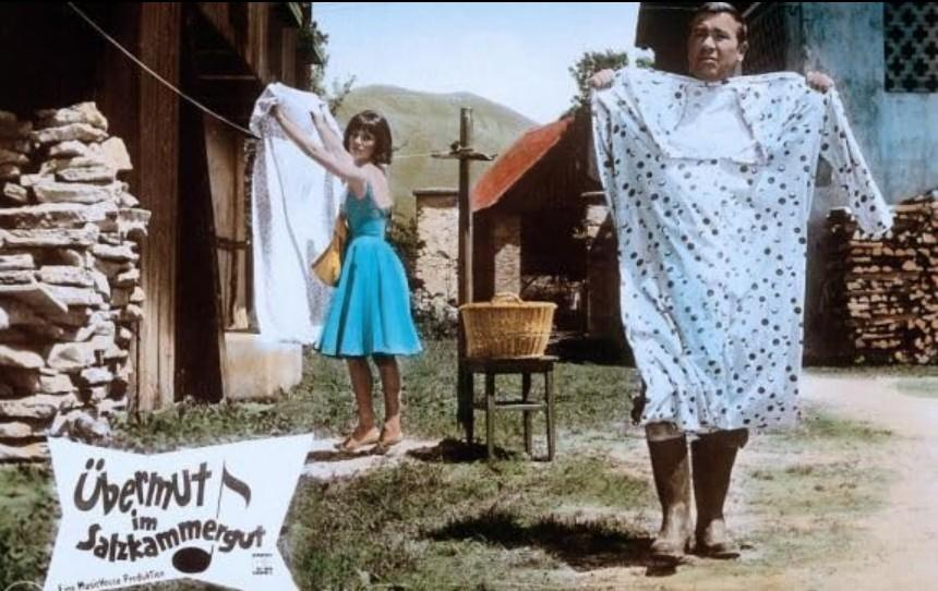 Mann hält ein groes gepunktetes Kleid; Frau hängt Wäsche auf.