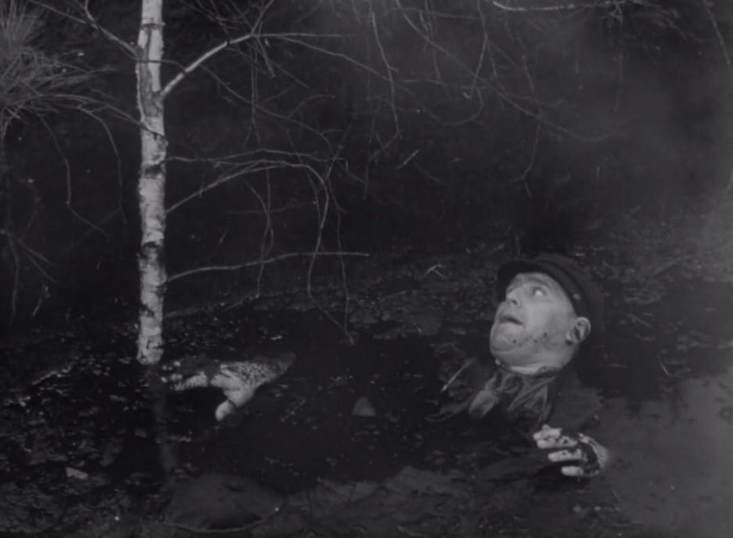 Ein Mann steckt bis zum Hals in schlammigem Wasser, neben einem Baum.