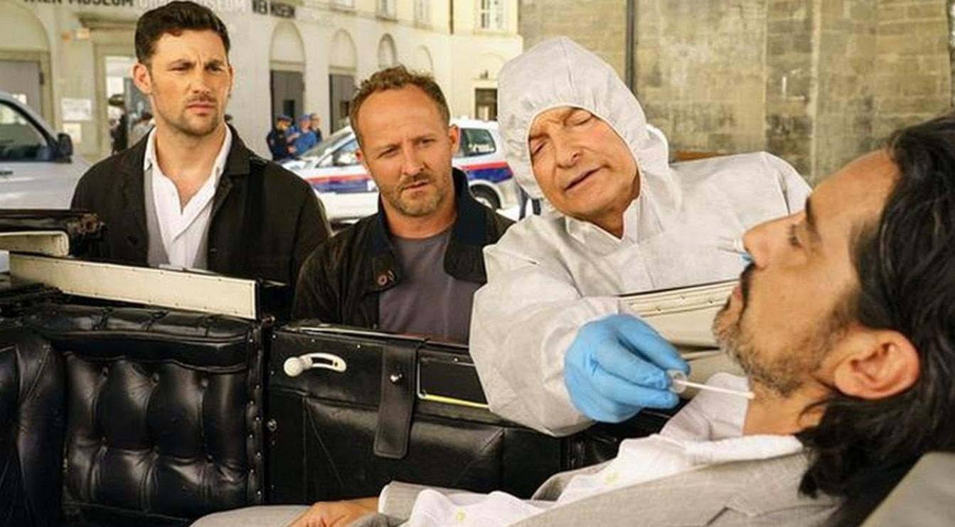 Ein Mann in Schutzkleidung entnimmt Proben von einem anderen Mann, während zwei Männer daneben stehen.