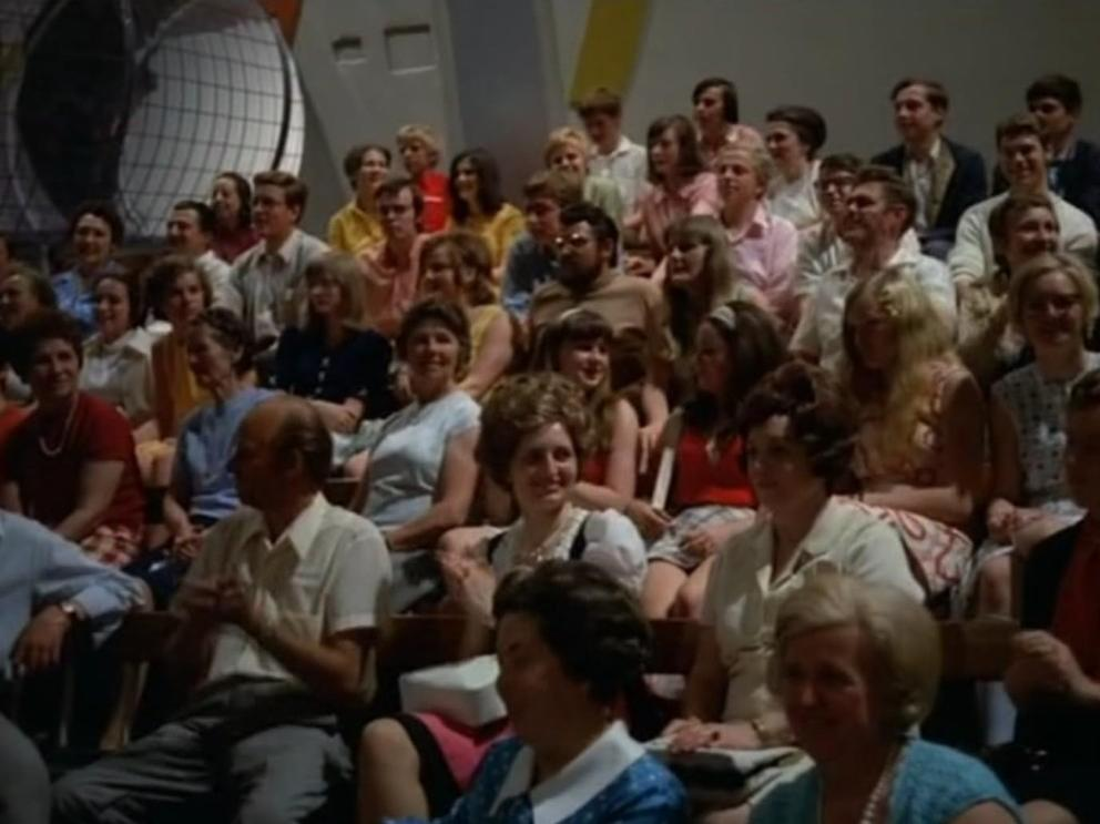 Eine Gruppe von Menschen sitzt in einem Auditorium, einige schauen nach vorne.