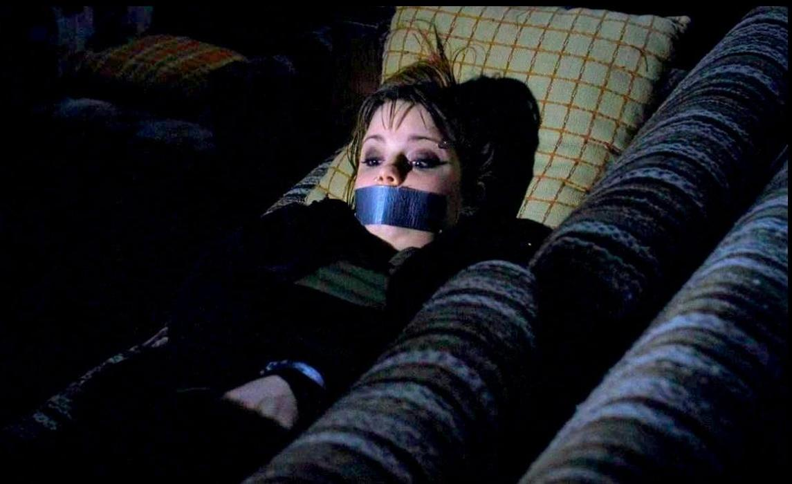 Eine junge Frau mit Klebeband über dem Mund liegt auf einem Sofa.