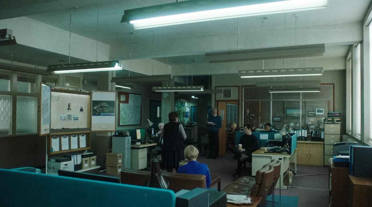 Büro mit Schreibtischen, Computern und Personen, die arbeiten oder sich unterhalten.
