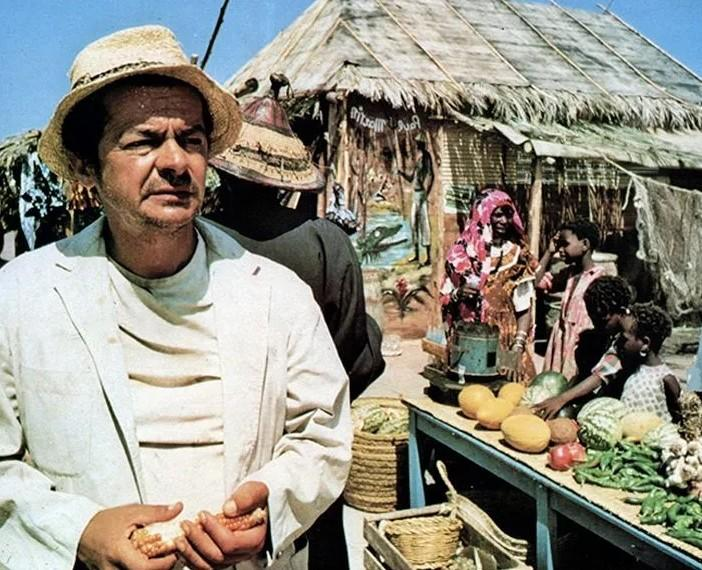 Ein Mann mit Strohhut auf einem Markt mit Obst, Gemüse und Hütten.