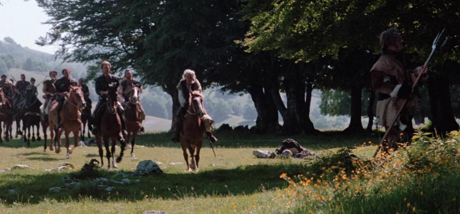 Eine Gruppe von Männern auf Pferden reitet durch eine grüne Landschaft unter Bäumen.