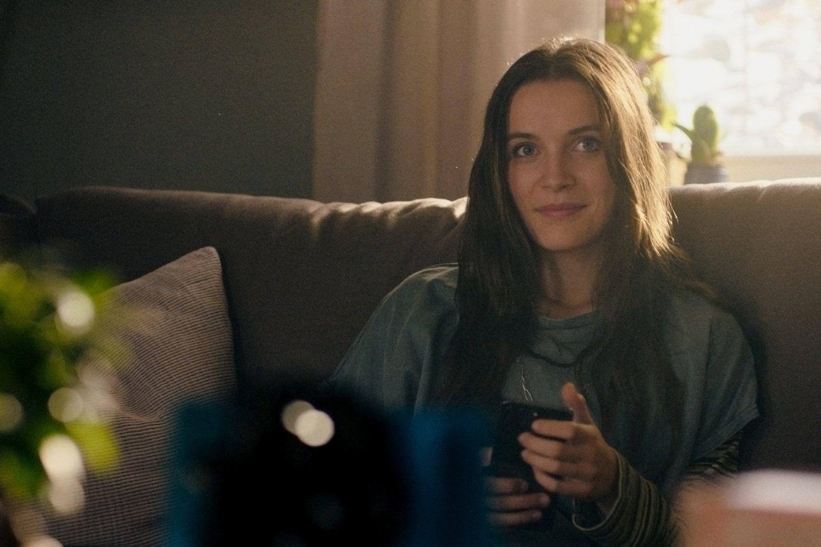 Eine Frau sitzt auf einem Sofa und hält ein Smartphone in der Hand.