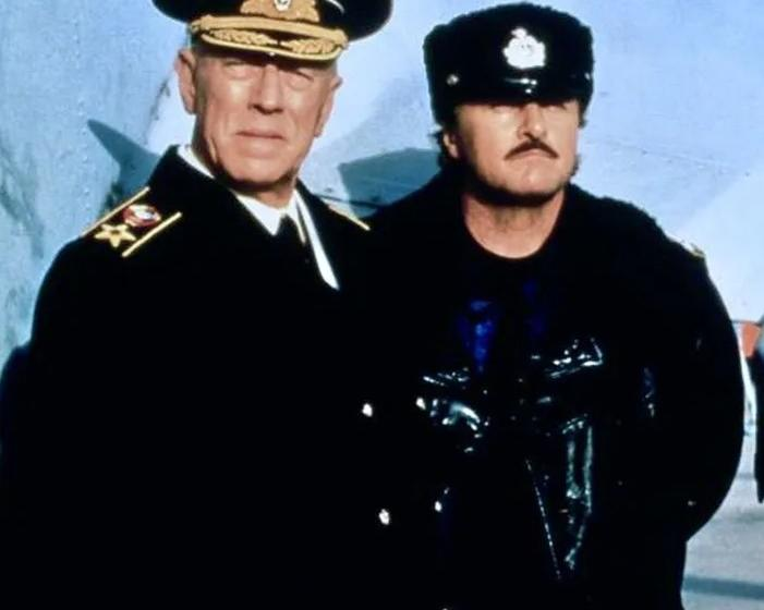 Zwei Männer in Uniformen, einer mit Mütze und Schnurrbart, stehen nebeneinander.
