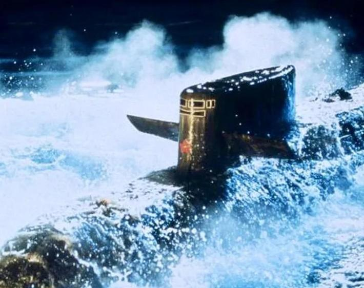 Ein U-Boot fährt durch raue, weiße Wellen unter blauem Himmel.