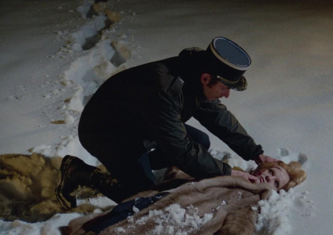 Ein Mann in Uniform kniet im Schnee neben einer Frau in einem Pelzmantel.