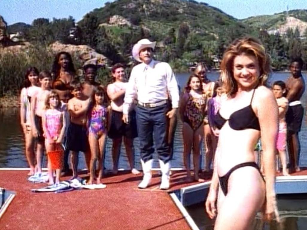 Eine Gruppe von Menschen steht auf einer roten Plattform am Wasser. Ein Mann trägt einen Cowboyhut.