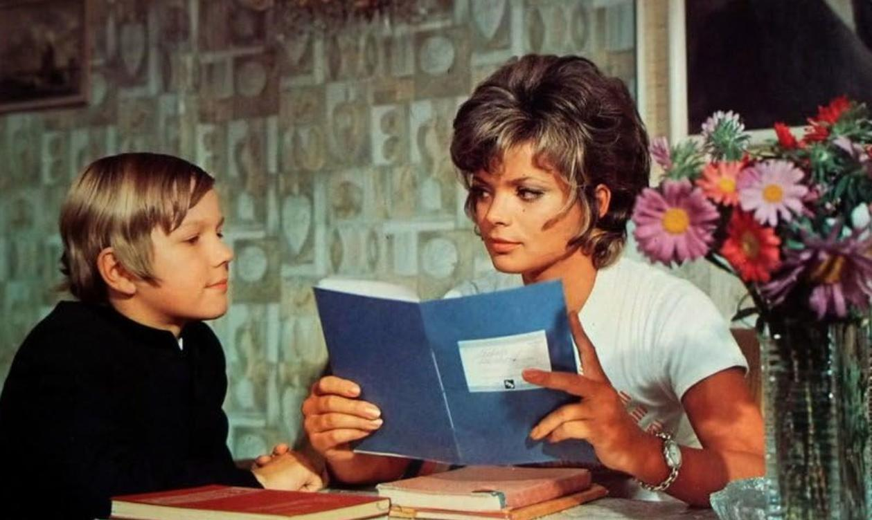 Eine Frau und ein Junge sitzen an einem Tisch und lesen. Im Hintergrund ist eine Vase mit Blumen.