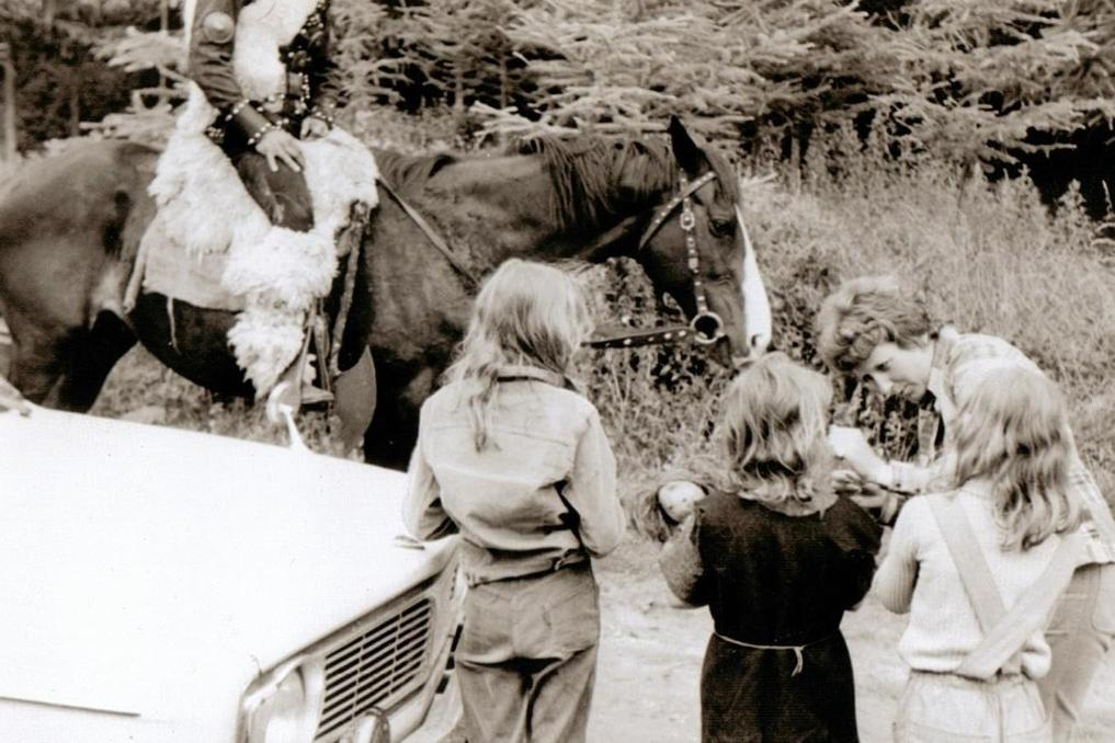 Reiter auf Pferd, Kinder und eine Frau stehen neben einem Auto im Wald.
