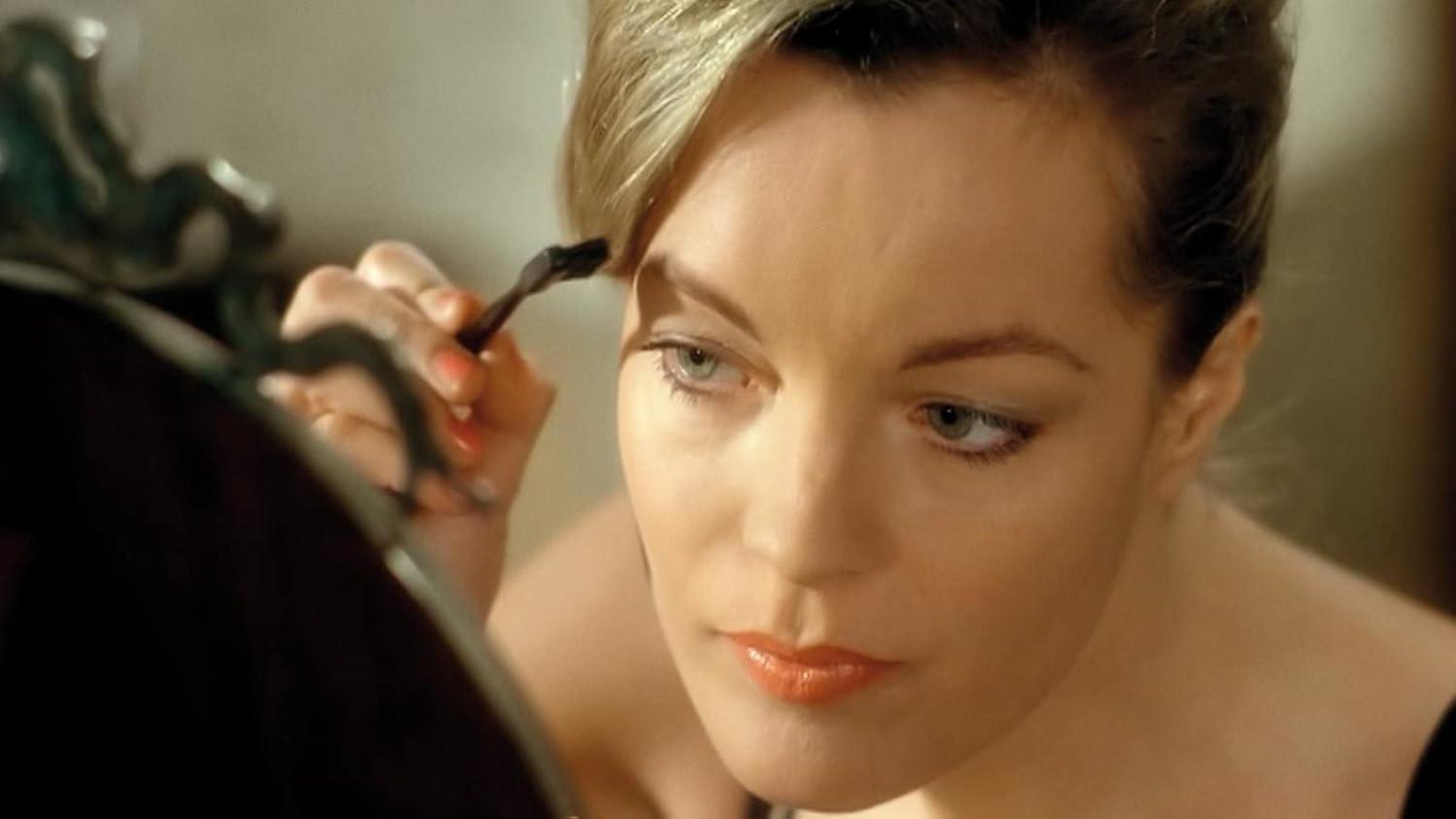 Eine Frau mit blondem Haar trägt Make-up auf, blickt in einen Spiegel.