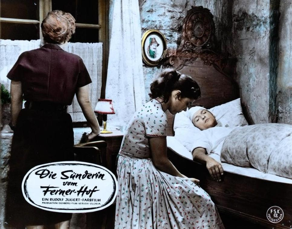 Eine Frau beugt sich über eine kranke Person im Bett. Eine andere Frau steht daneben.