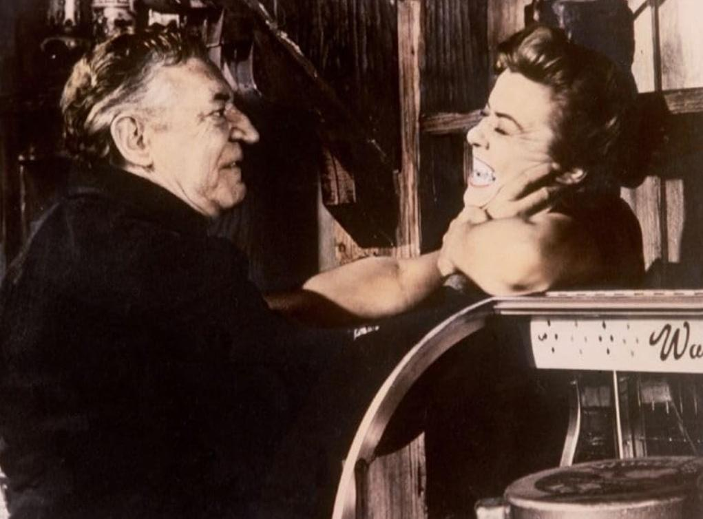 Ein Mann mit dunklem Hemd greift einer Frau mit heller Kleidung an den Hals.