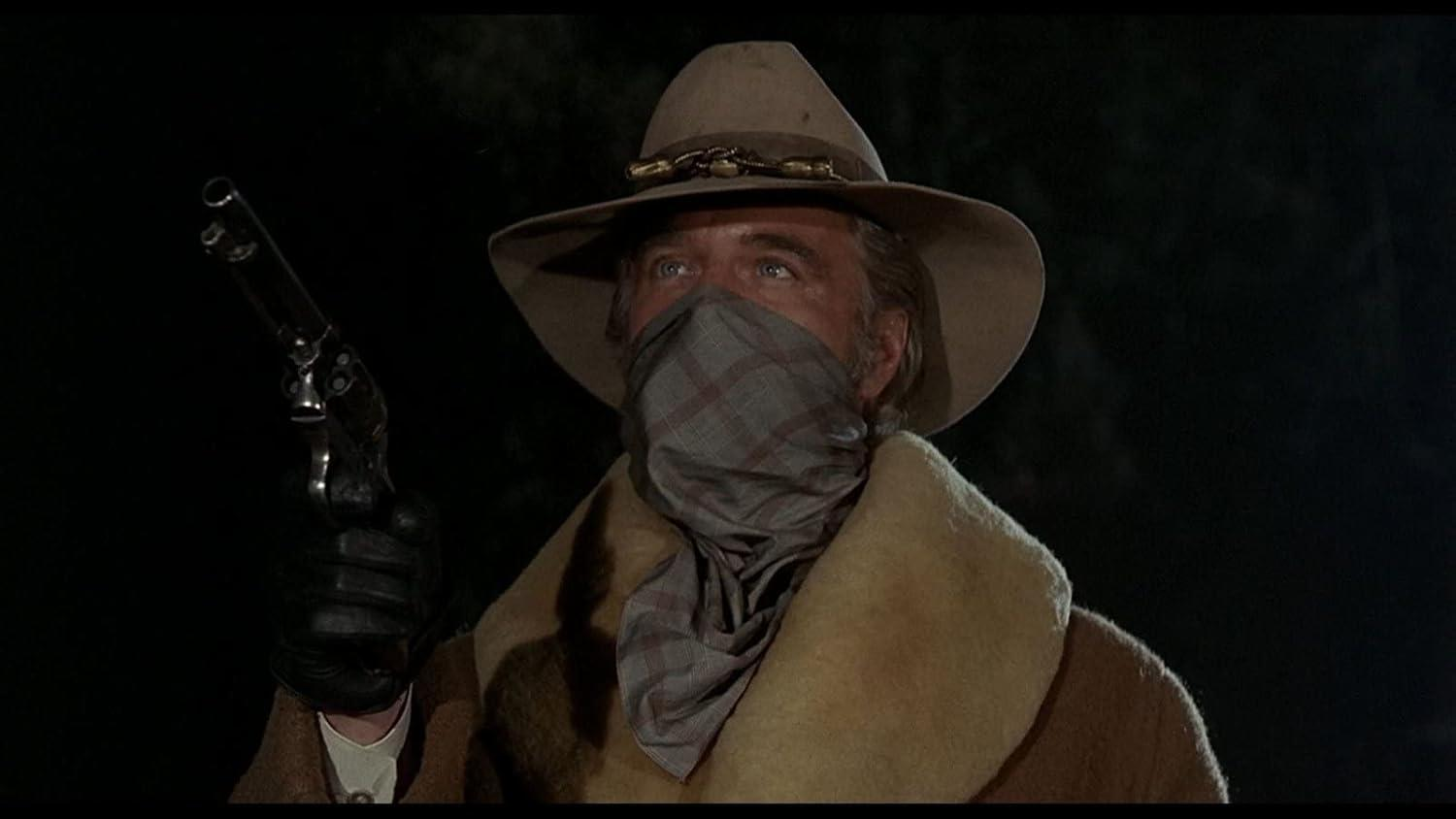 Ein Mann mit Cowboyhut und Bandana hält eine Waffe und blickt zur Seite.