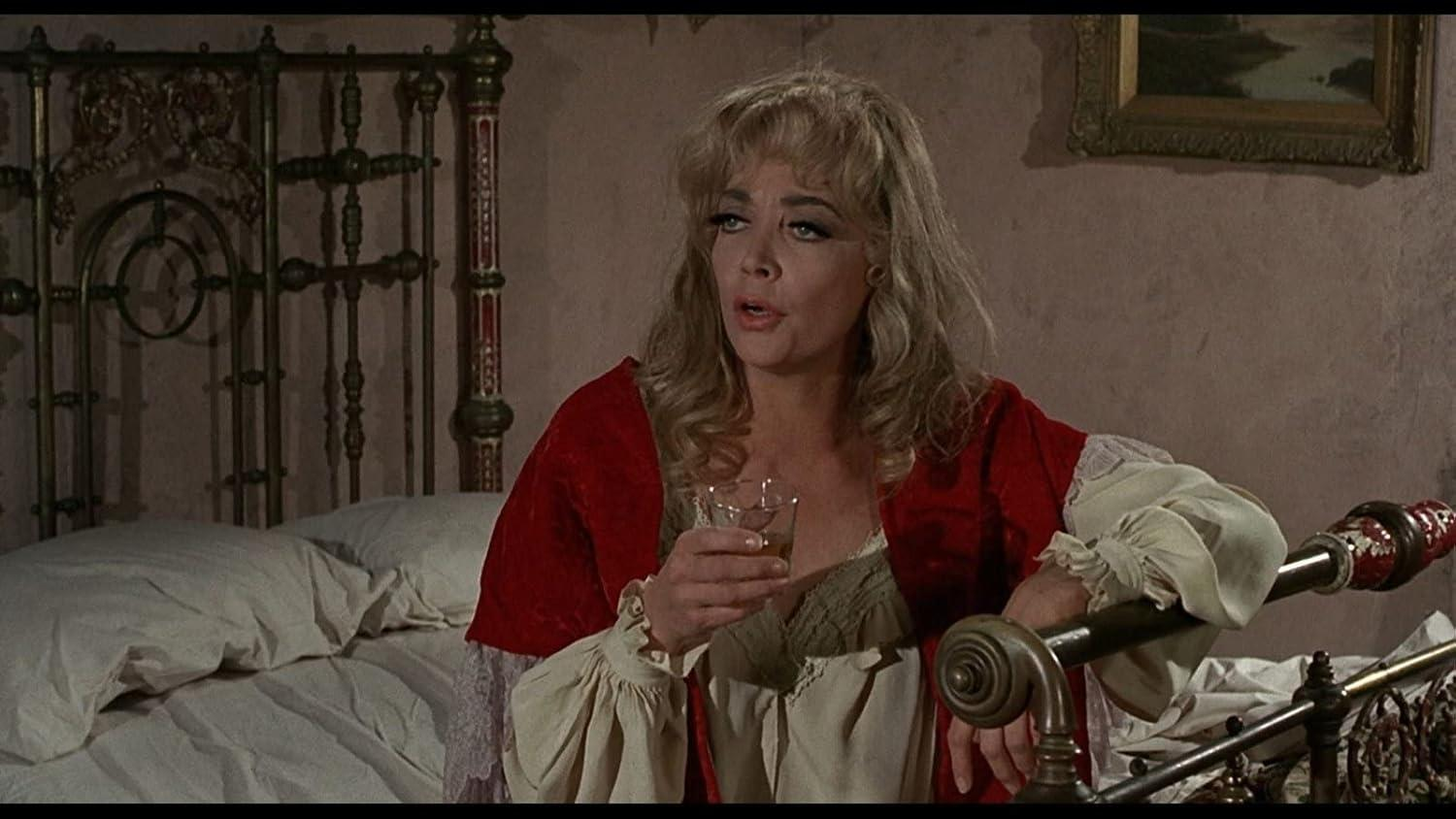 Eine Frau mit blonden Haaren in rotem Kleid hält ein Glas mit Getränk.