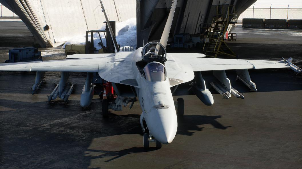Ein hellgraues Kampfflugzeug mit Raketen unter den Flügeln steht auf einem Flugzeugträgerdeck.