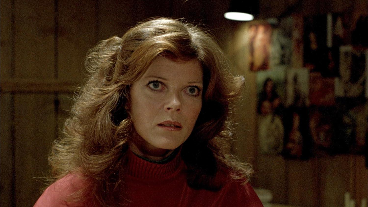 Eine Frau mit braunen Haaren trägt einen roten Pullover, ihr Blick ist besorgt.