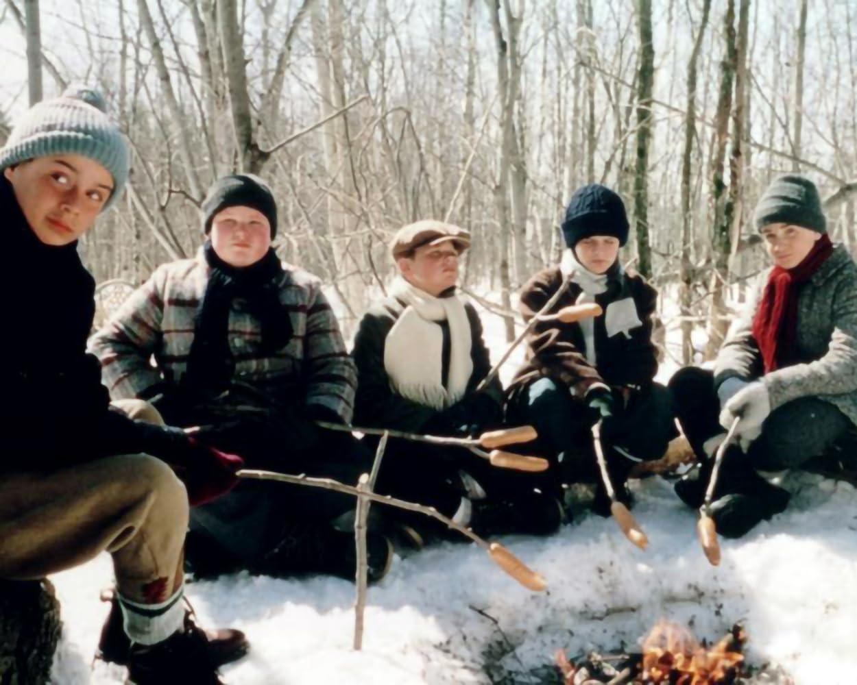 Fünf Jungen braten Würstchen über einem Lagerfeuer im Schnee.