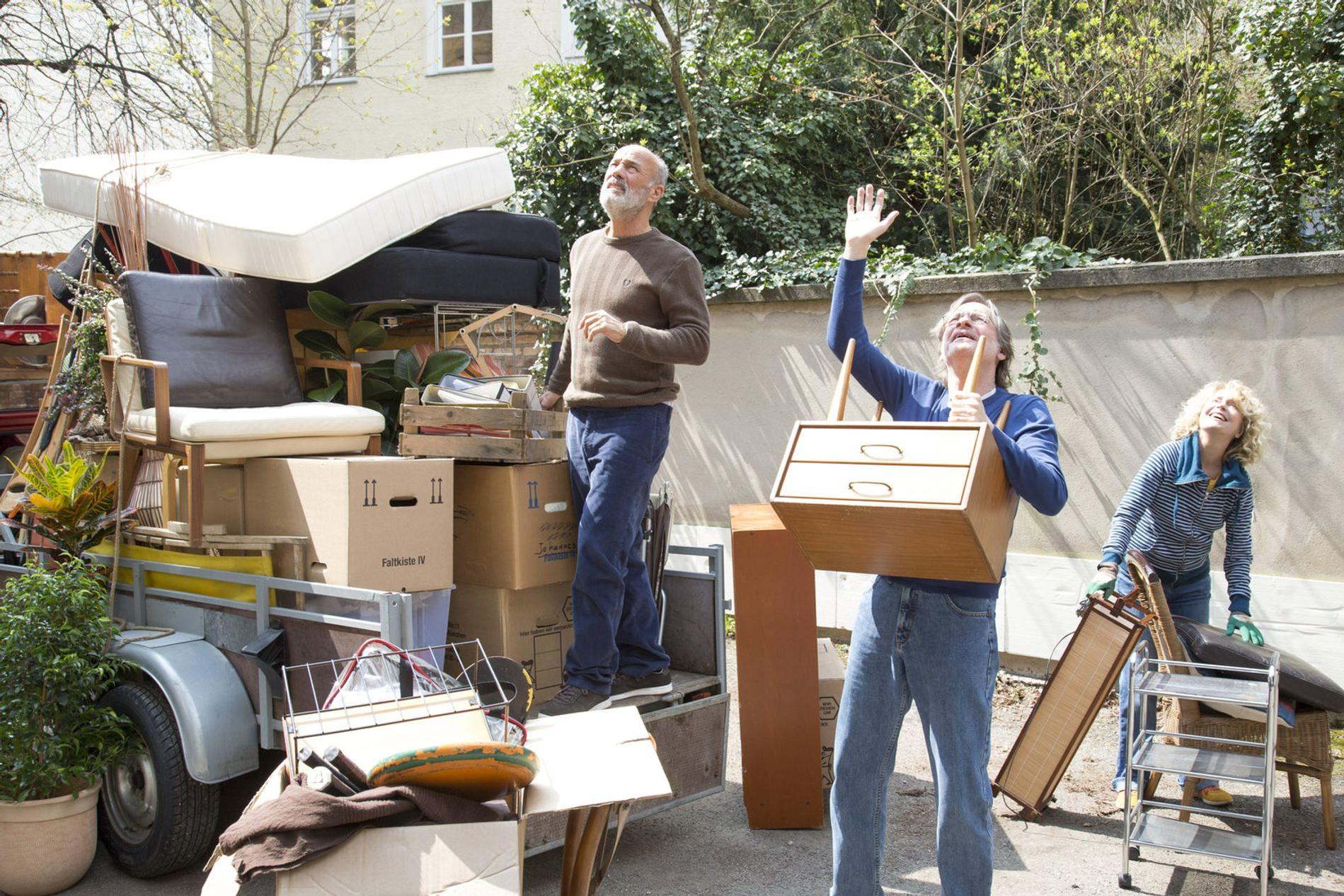 Menschen sortieren Möbel und Kisten vor einem Haus.