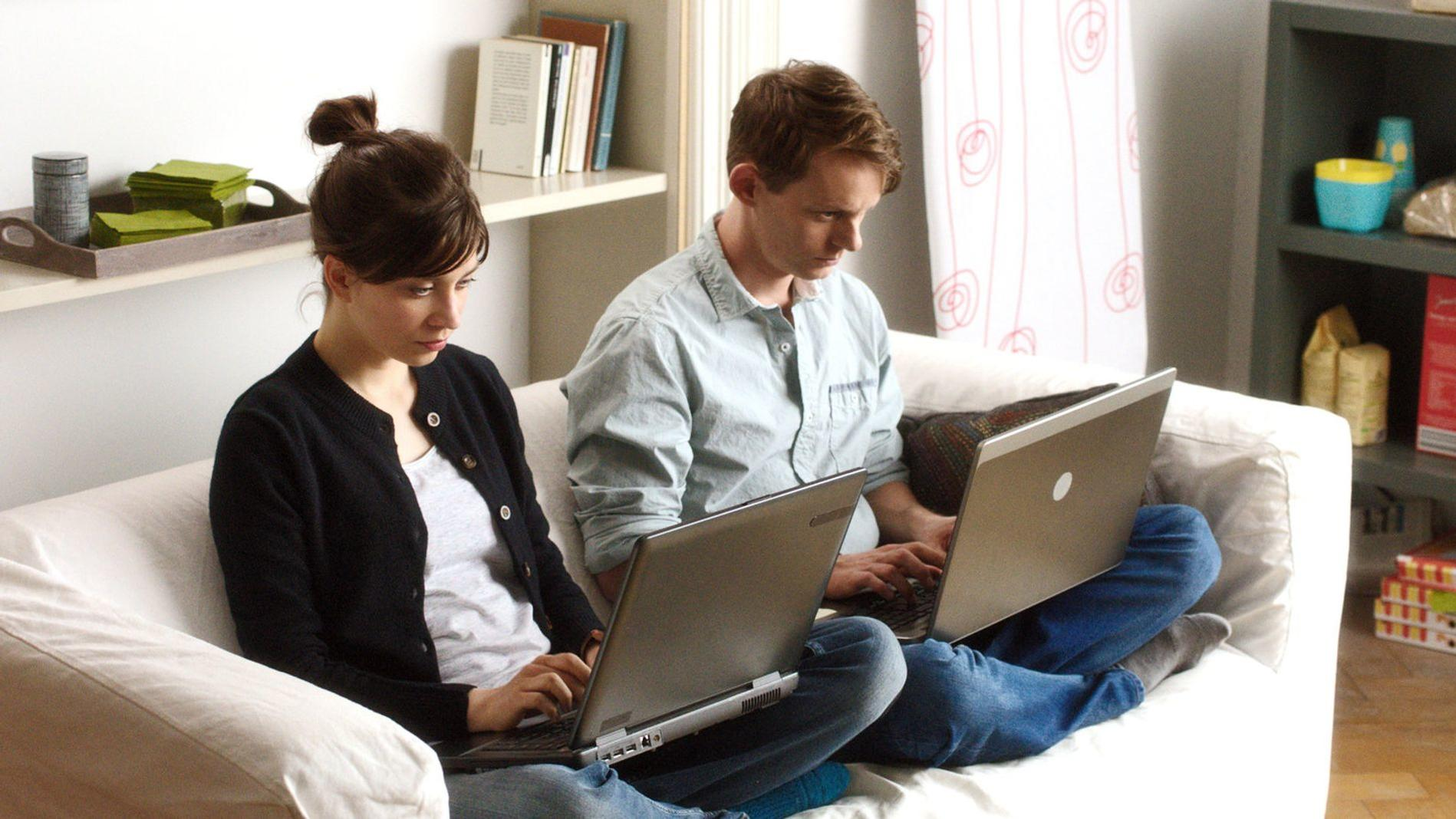 Zwei Personen sitzen auf einem Sofa und benutzen Laptops.