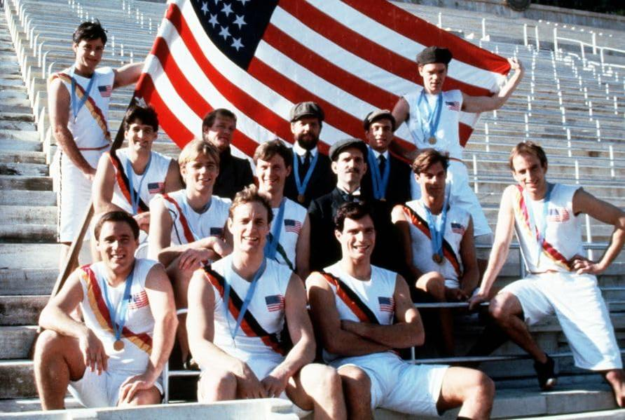 Ein Team von Athleten in weißer Kleidung mit Medaillen und einer US-Flagge.
