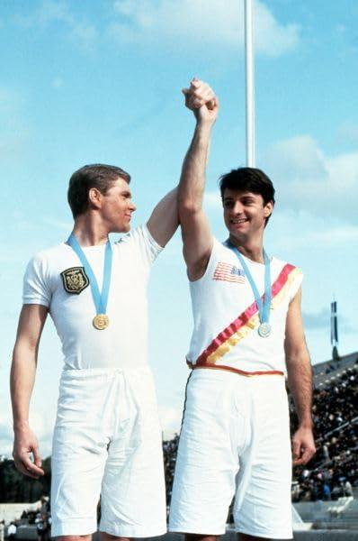 Zwei Athleten stehen mit Medaillen auf einem Podium, einer hebt den Arm seines Partners.