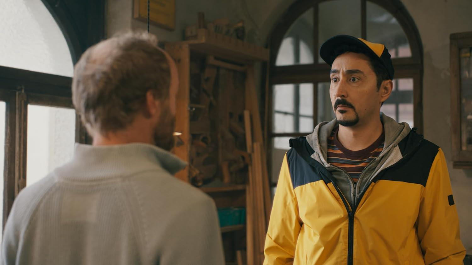 Ein Mann in einer gelben Jacke spricht mit einem Mann, dessen Rücken zu sehen ist.