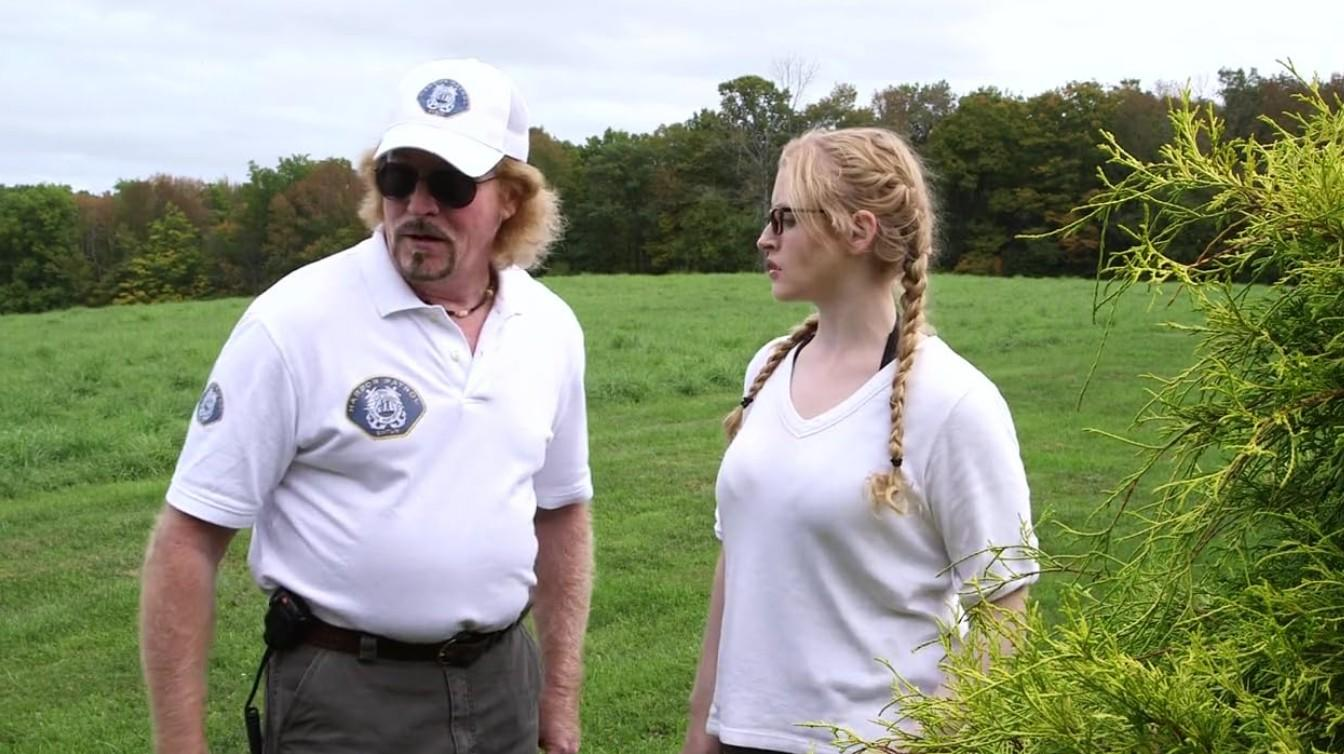Mann und Frau stehen auf einer grünen Wiese mit Bäumen im Hintergrund.