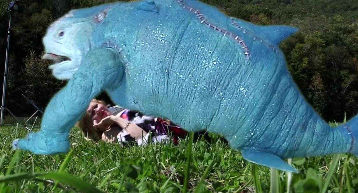 Ein blaues Monster mit Armen und Beinen auf einer Person im Gras.