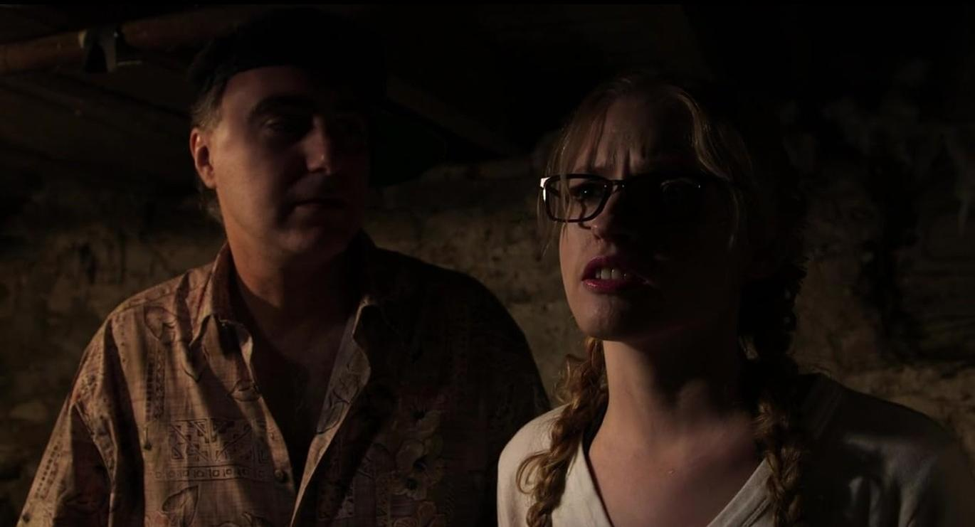 Mann mit Baskenmütze und Frau mit Brille in dunkler Umgebung.