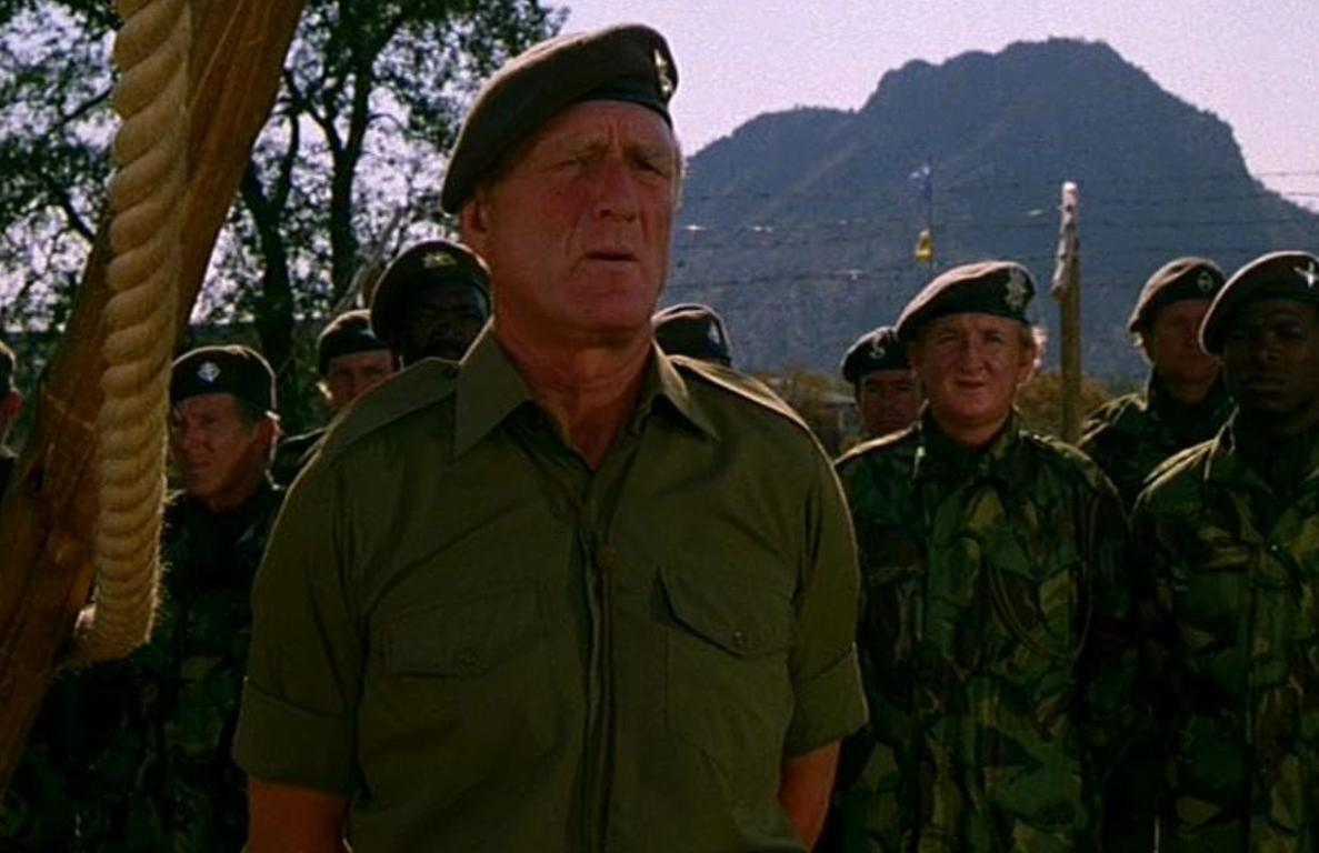 Militärangehörige in Tarnuniform und Baretts stehen vor einem Berg.