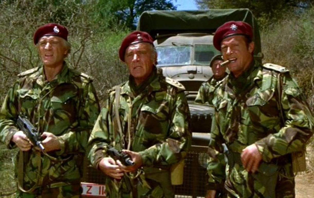 Drei Soldaten in Tarnuniformen und roten Baretts stehen vor einem Militärlastwagen.