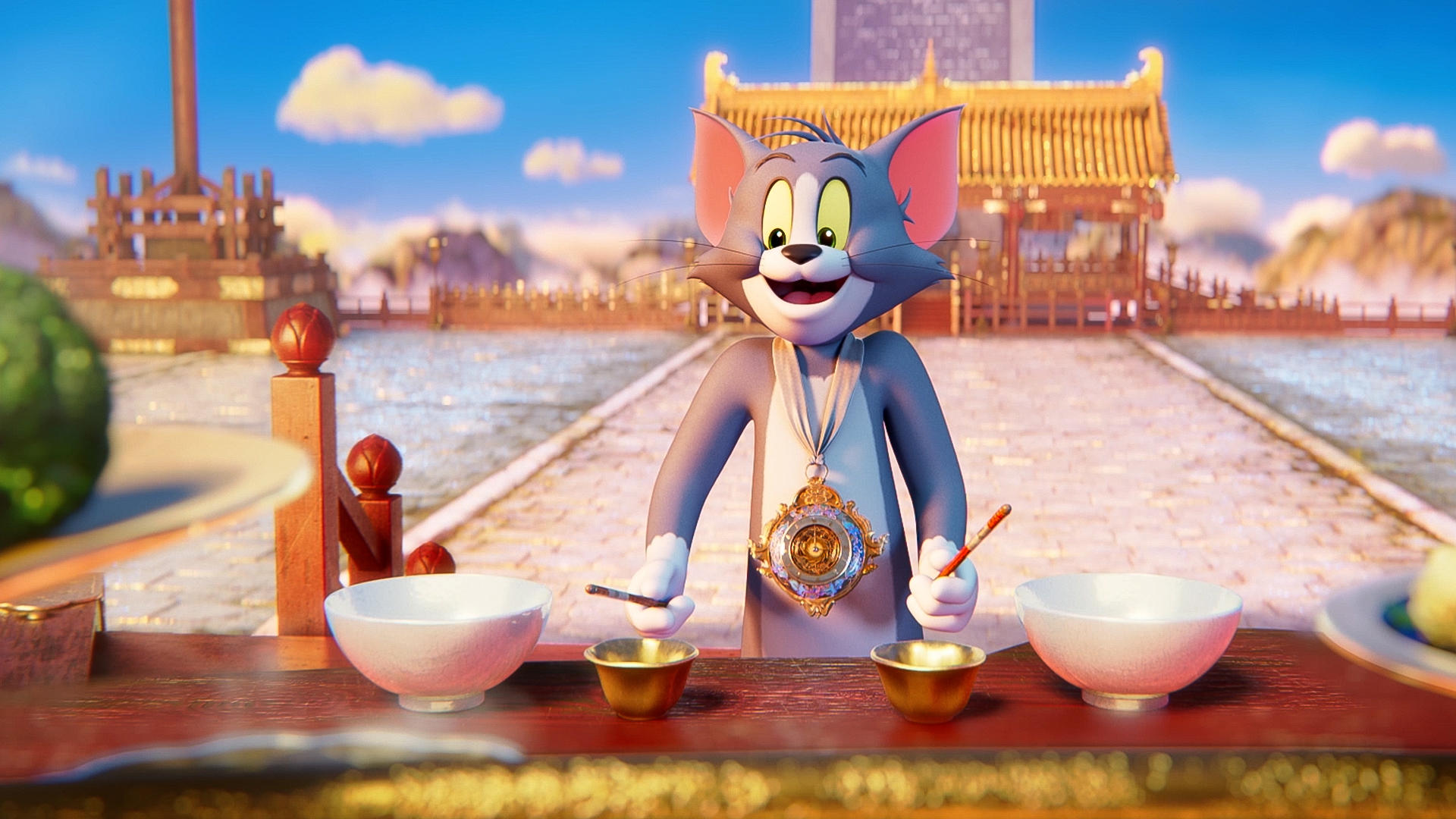 Tom der Kater steht vor einer asiatischen Pagode und hält Essstäbchen.