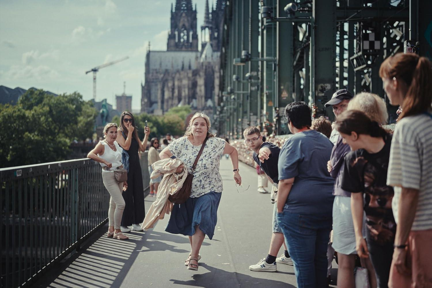 Menschen auf einer Brücke vor einer Kathedrale, eine Frau rennt.