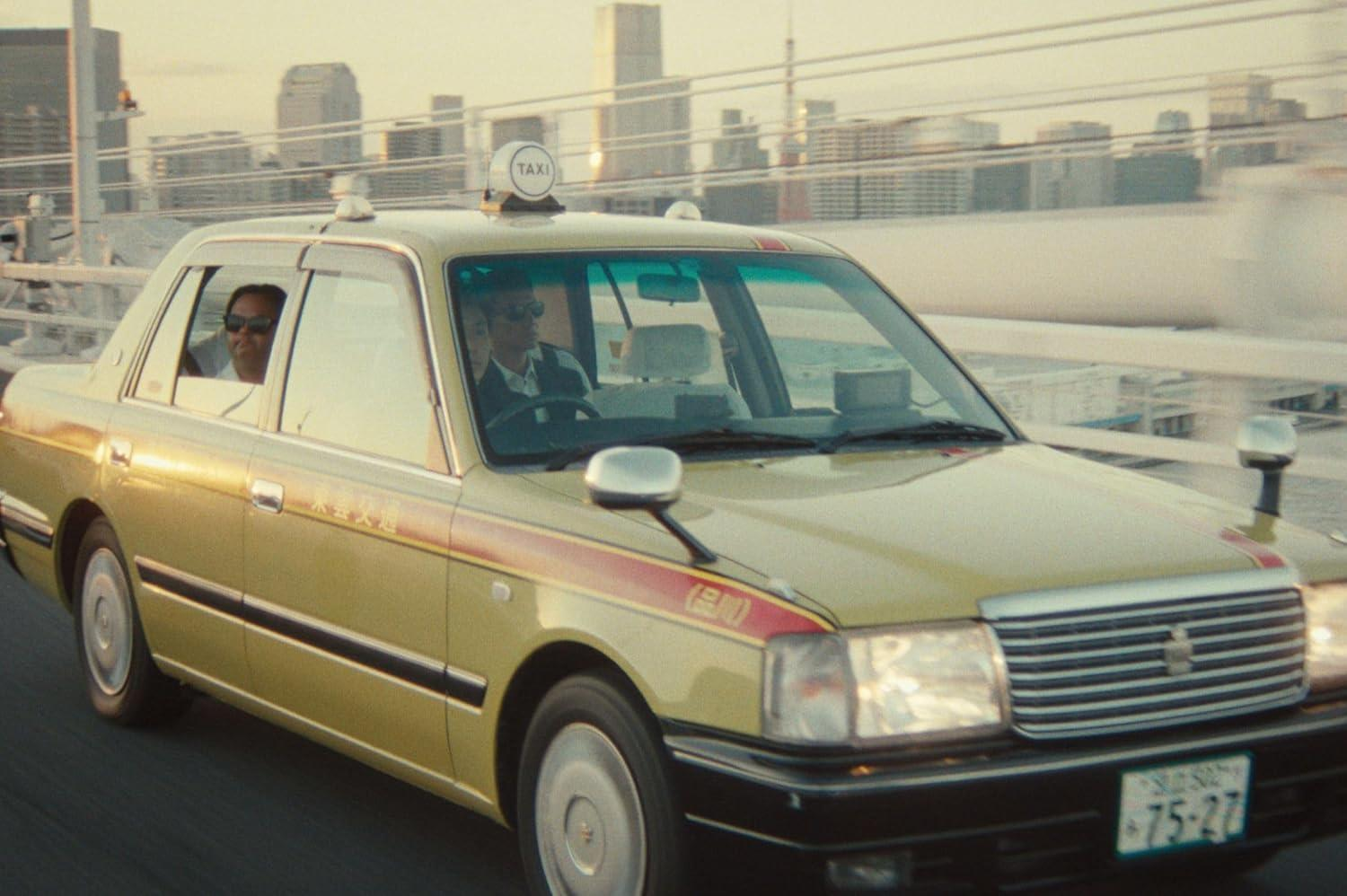 Ein gelber Taxi mit Fahrgästen fährt auf einer Brücke mit Stadtkulisse im Hintergrund.